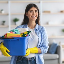 Young housewife holding bucket with cleaning supplies tools